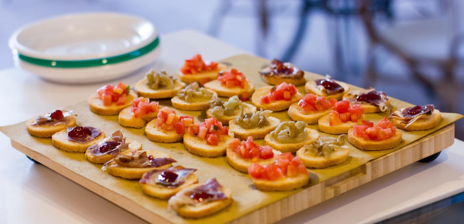 Crostini assortiti con pomodori, patè e marmellata su tagliere di legno.