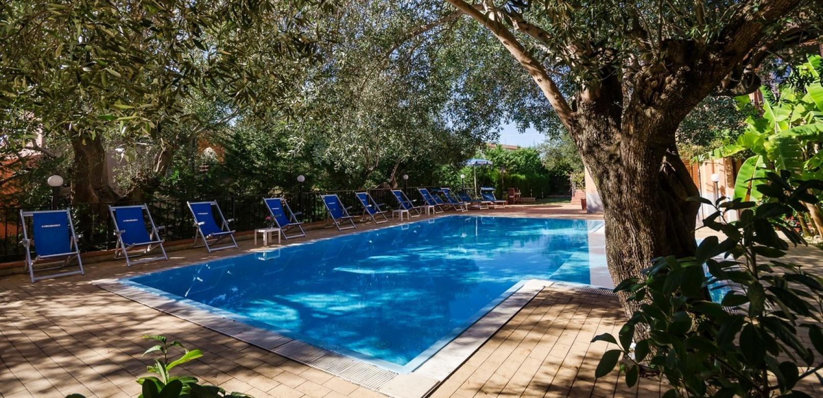 Piscina all'aperto circondata da alberi e sedie a sdraio blu.