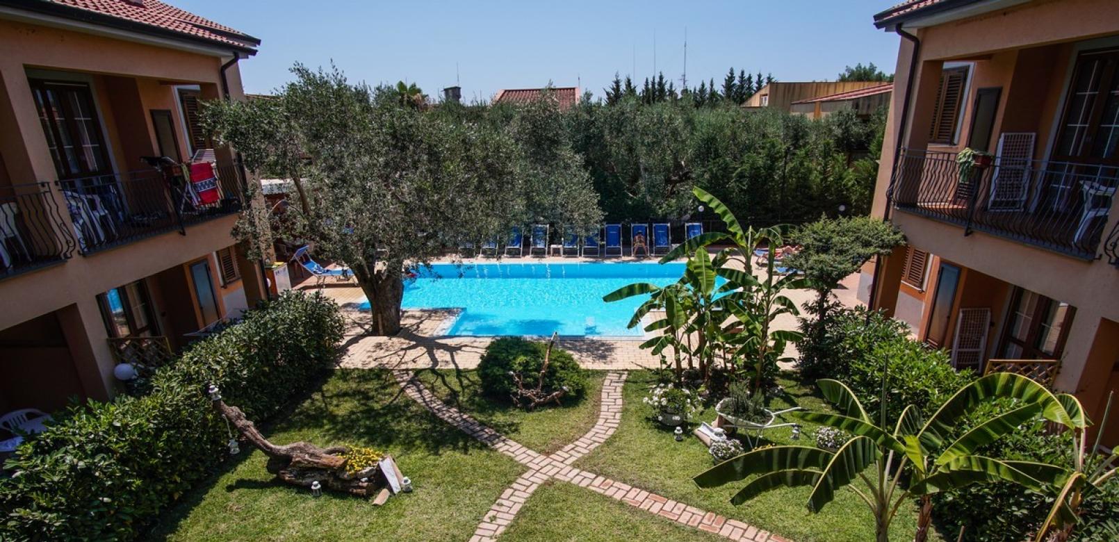 Giardino con piscina, sentieri in mattoni, vegetazione rigogliosa e sedie a sdraio.