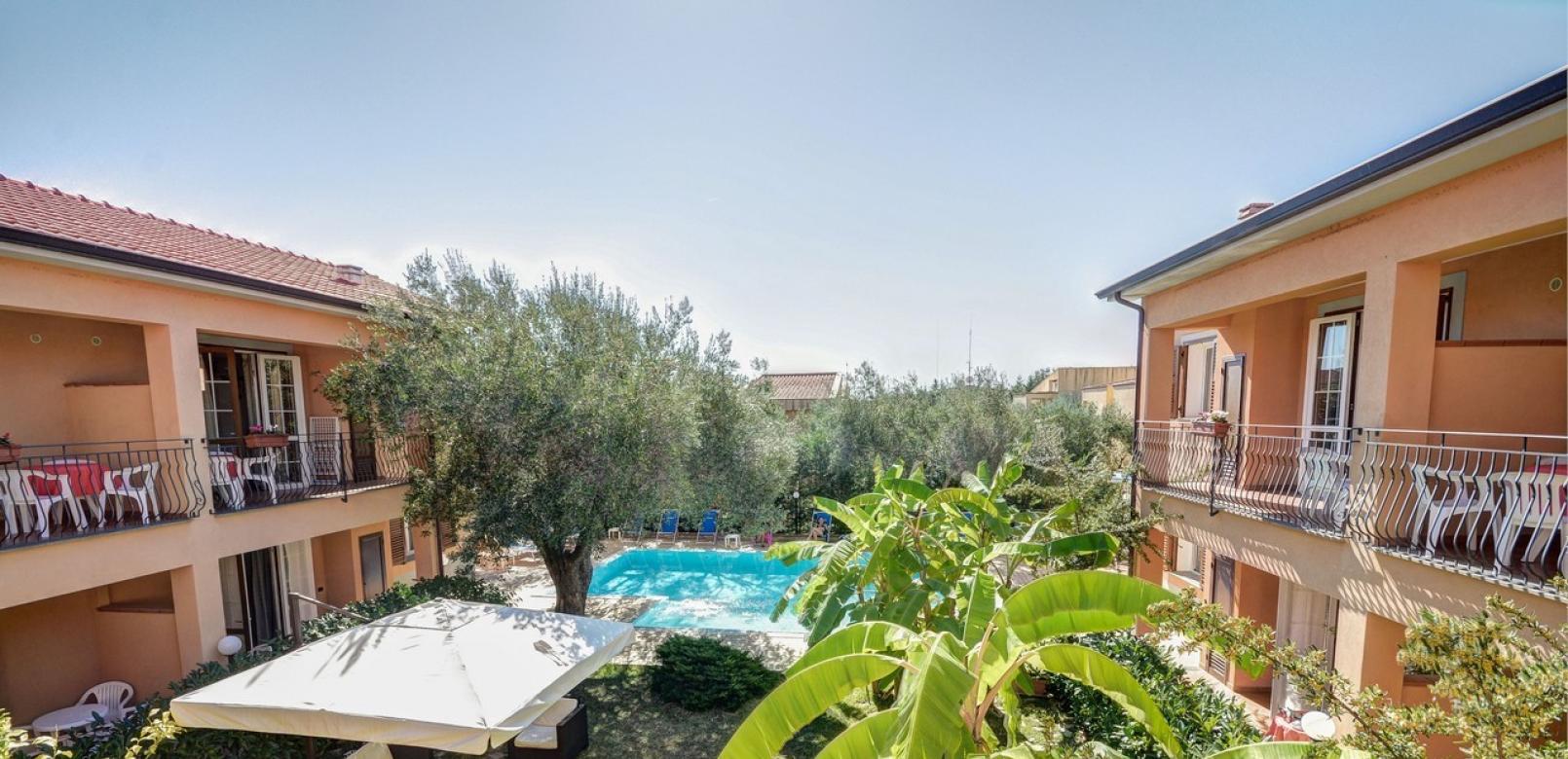 Complesso residenziale con piscina, giardino e area relax, circondato da vegetazione rigogliosa.