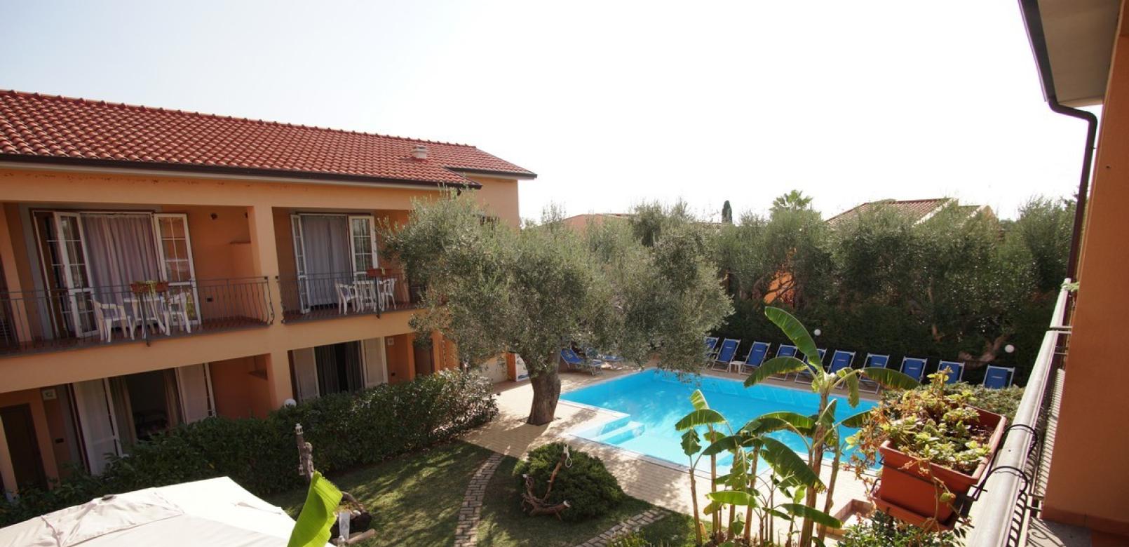 Giardino con piscina, sedie a sdraio e balconi in un ambiente mediterraneo.