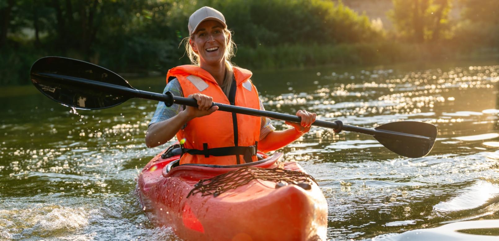 Persona in kayak su un fiume, indossa un giubbotto di salvataggio arancione.