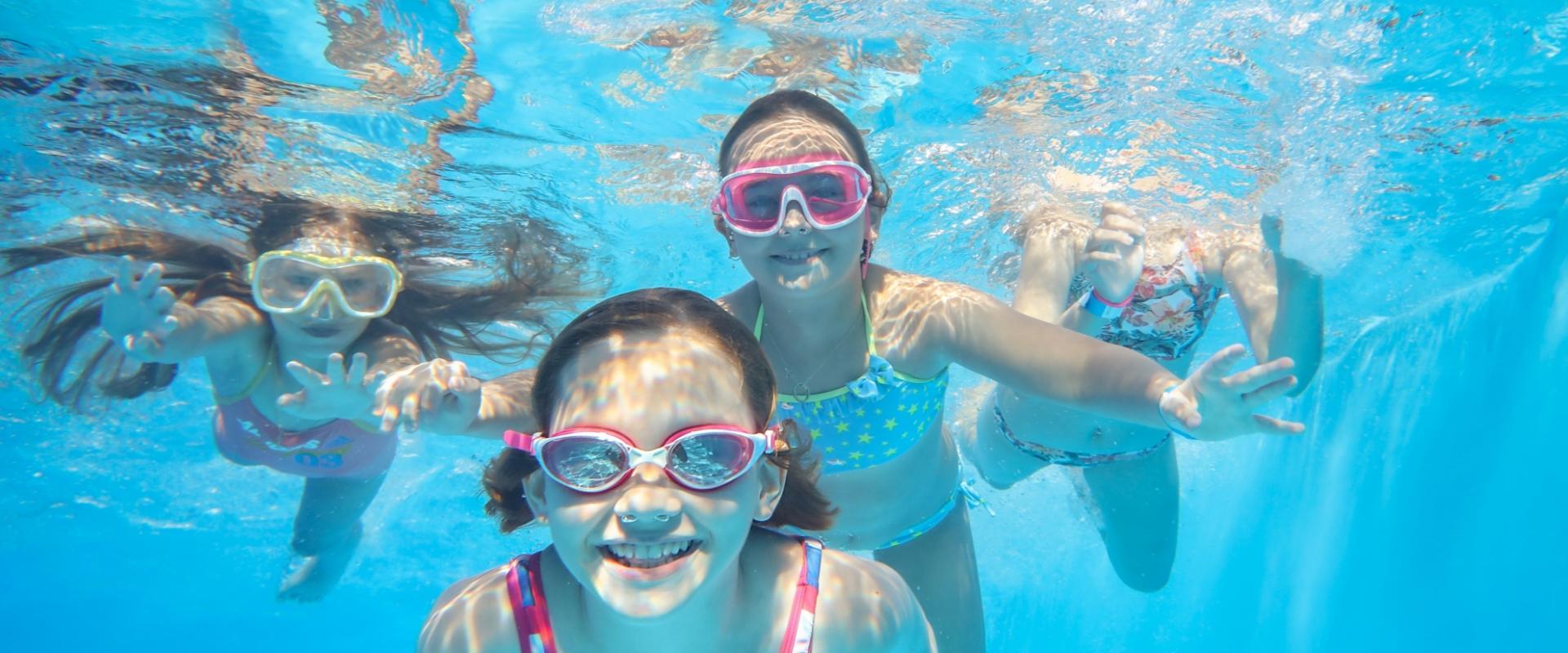 Bambini sorridenti nuotano sott'acqua con occhialini colorati in piscina.