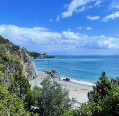 Spiaggia panoramica con mare azzurro e scogliere, cielo sereno e vegetazione verde.