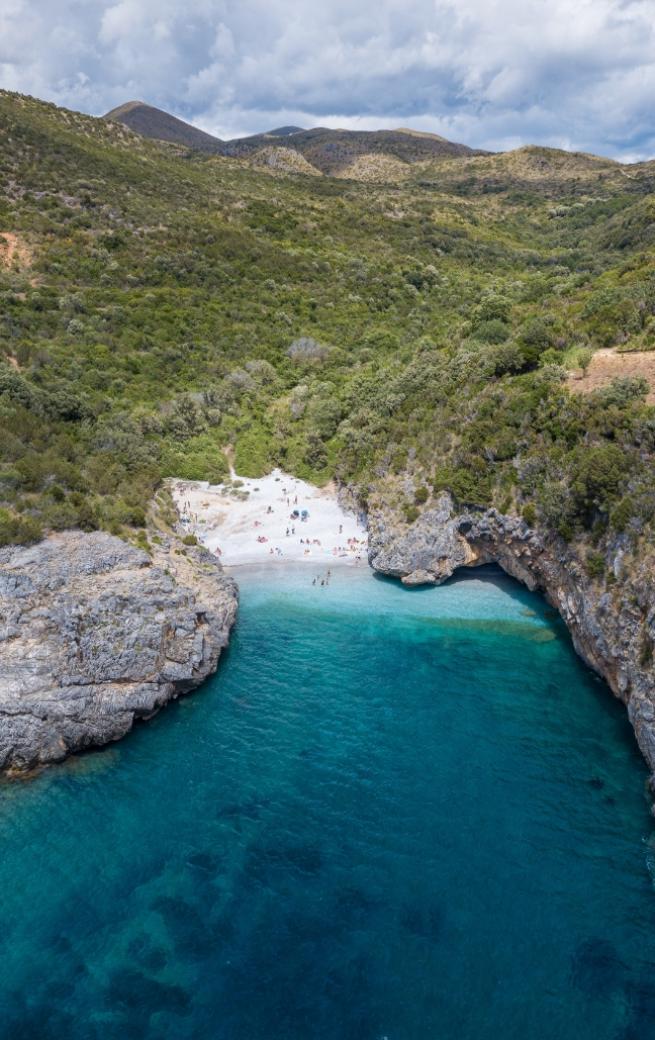 Spiaggia nascosta tra scogli e vegetazione, con mare cristallino e sabbia bianca.