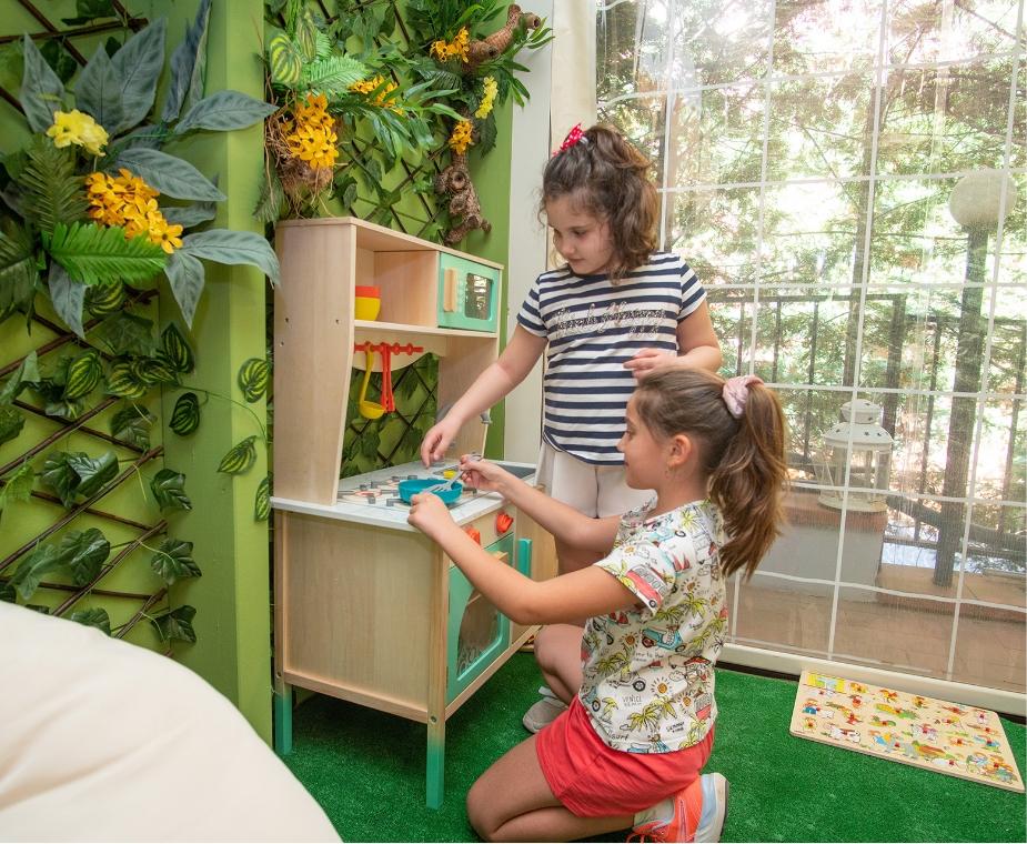 Due bambine giocano in una cucina giocattolo in un ambiente verde e naturale.